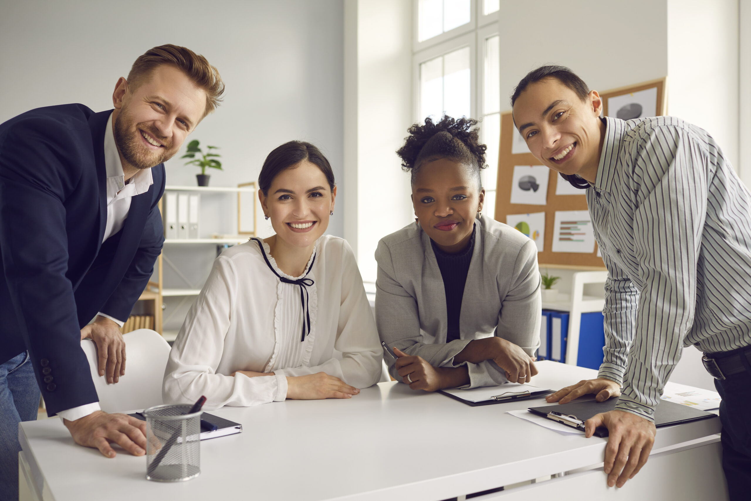 International company, teamwork, brainstorming concept. Positive multiethnic office workers sitting in office discussing corporate project and looking at camera together